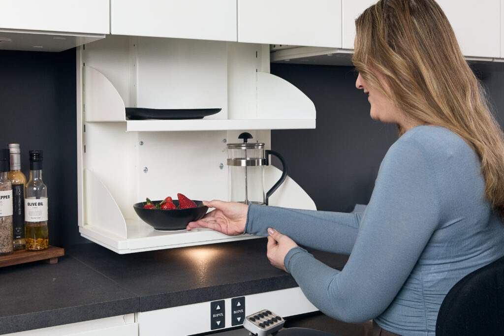 Wheelchair user reaching items from a Ropox VertiInside cabinet with shelves lowered to countertop height