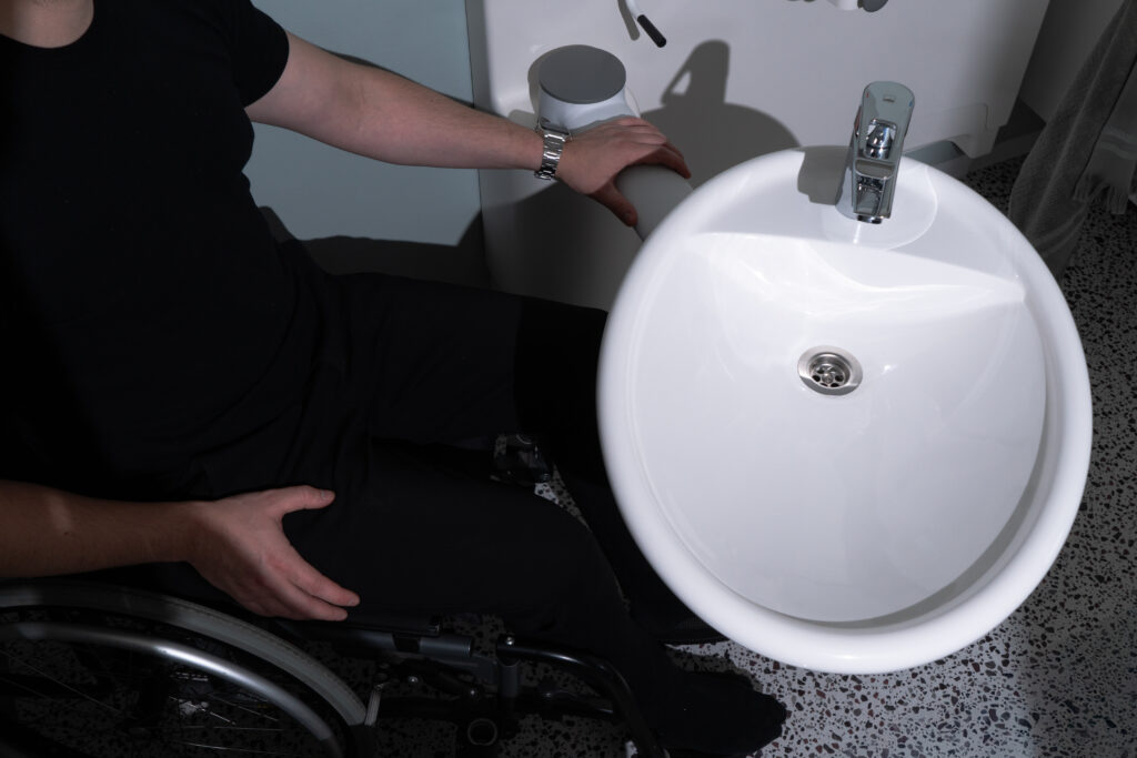 Wheelchair user beside a Ropox SwingLine washbasin rotated outward for access